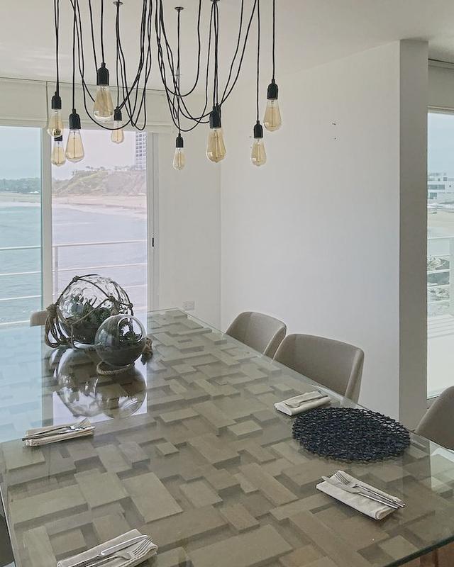 Dining table of oak blocks under glass, bare-bulb pendants on black cables, the beach through the window