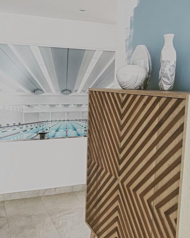 A chevron oak cabinet with three marbled vases against a blue painted wall, a photograph of a swimming pool beyond