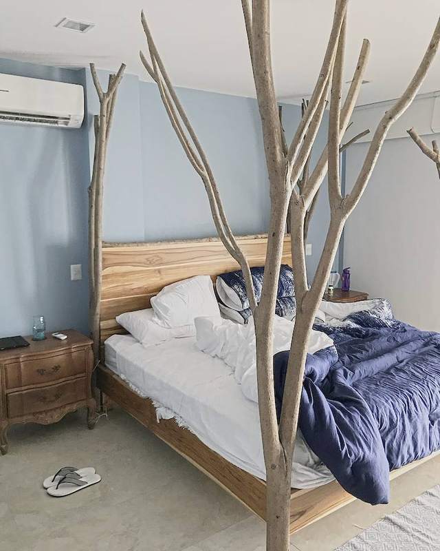 A bed of solid wood framed by four bare tree trunks against a pale blue wall