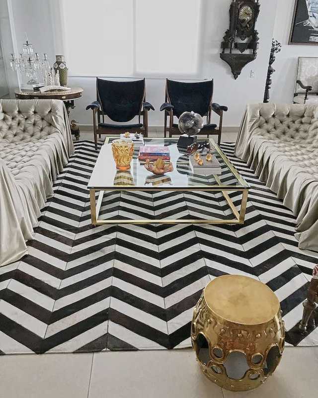 Draped tufted sofas, two dark armchairs and a brass and glass table on a black and white chevron hide rug