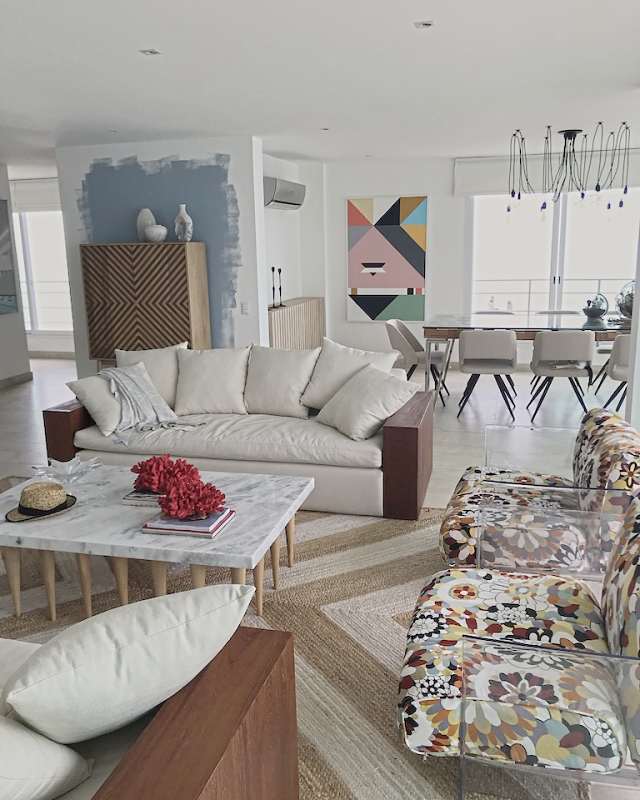Two white sofas in red-wood frames, Missoni-print armchairs in clear acrylic, a chevron jute rug and the sea beyond