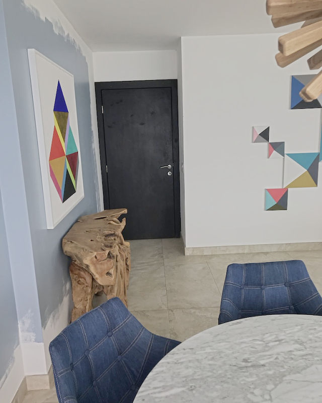 A teak root console under a geometric work on a blue painted wall, a black door beyond