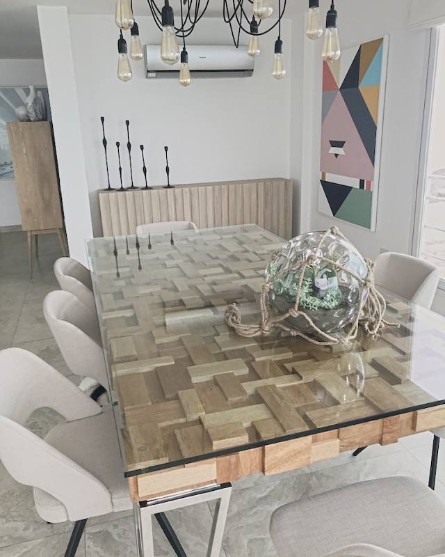Oak-block dining table under glass with a rope-bound glass terrarium, a jagged oak sideboard and iron candlesticks beyond