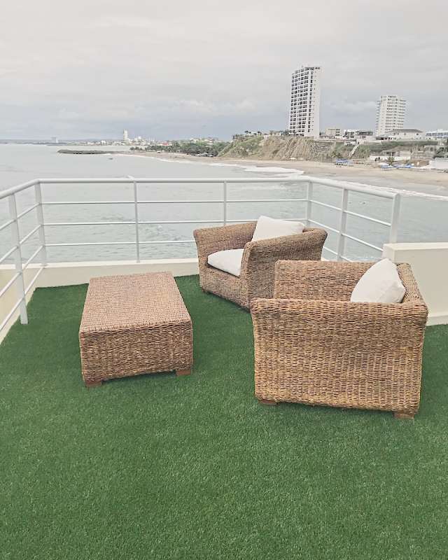 Two woven armchairs and an ottoman on the roof terrace, the beach and the bay behind