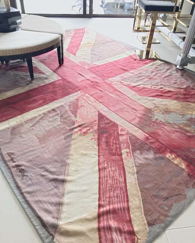 A woven flag rug in faded reds and creams beside gold bar stools