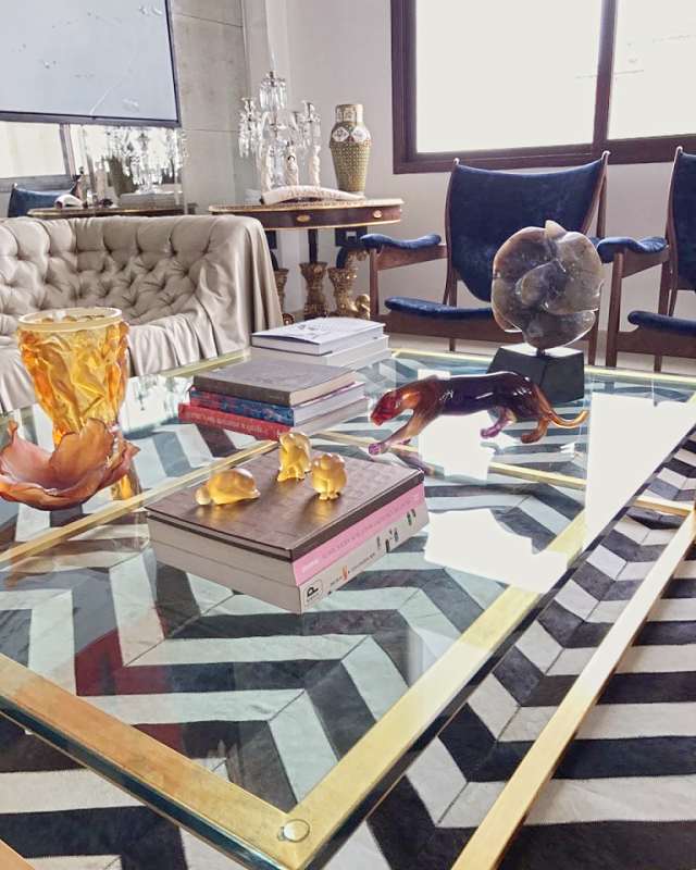 Close view of the brass and glass table with amber crystal, a stone sculpture and books, antiques behind