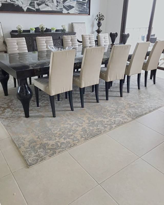The dining table and pale chairs on a grey and gold damask rug