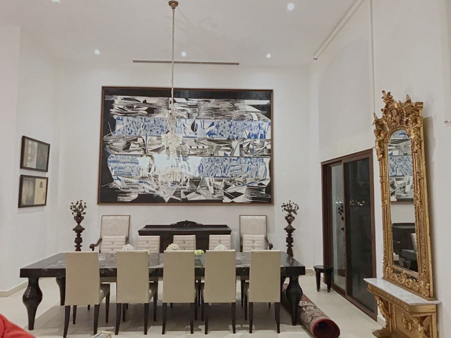 A double-height dining room: a black lacquer table for twelve, a large black, white and blue painting, a crystal chandelier and a gilded baroque mirror