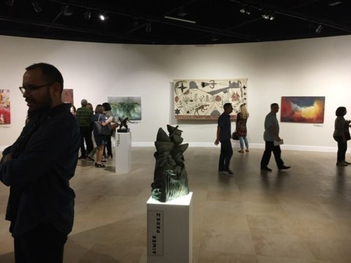 A gallery with José Bedia’s felt Semana Santa hanging on a curved wall, visitors and a sculpture on a plinth