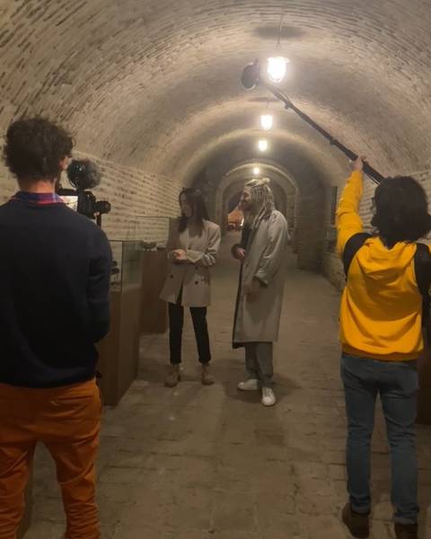 A film crew with camera and boom recording two people talking in a vaulted brick tunnel