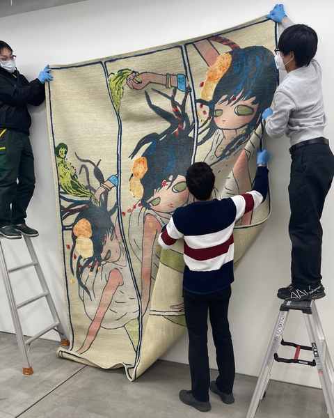 Three gallery staff in gloves hanging a large hand-knotted work from ladders