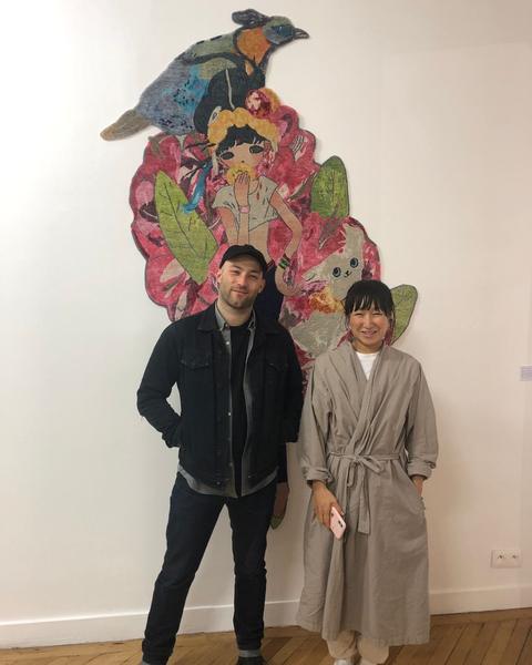 Aya Takano standing in front of a shaped hand-knotted work of a girl, a bird and a cat