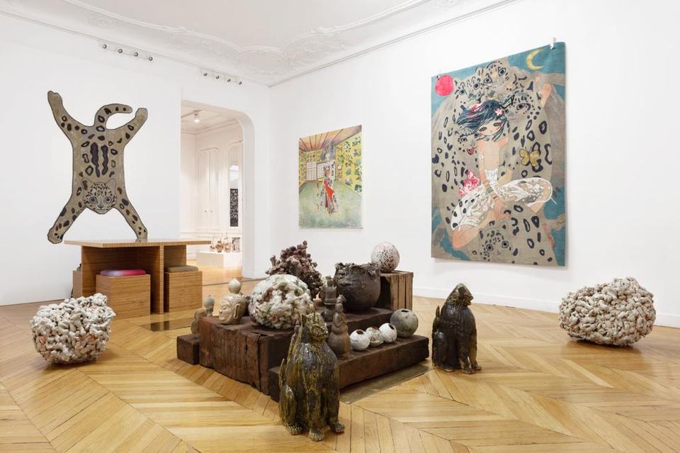 A gallery room with Aya Takano's hand-knotted works: a leopard-skin shaped piece and a large work of a girl among snow leopards on the walls, ceramics on wooden plinths