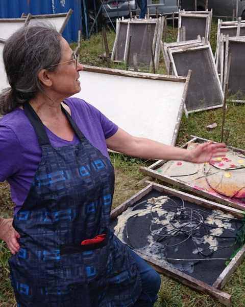 Jessica Stockholder in an apron gesturing toward her sheets among the drying moulds