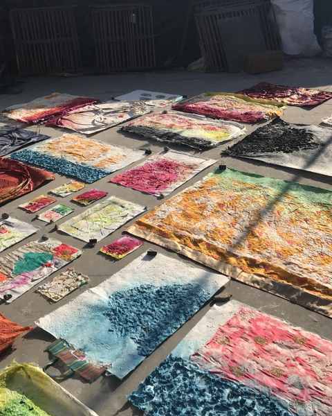 Dozens of finished lokta sheets in red, blue, black and yellow laid out to dry on a concrete floor