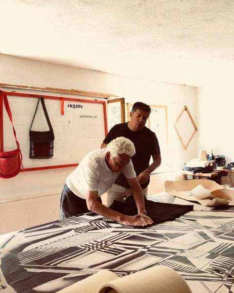 A master felt-maker pressing black wool onto a full-size drawing on the workshop table