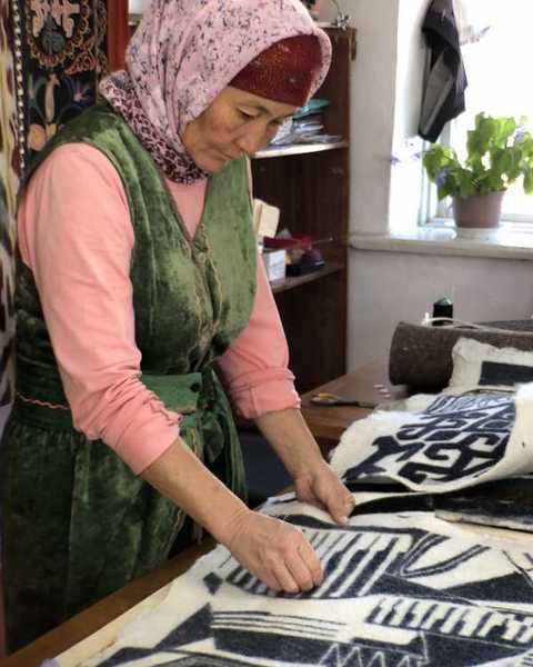 A felt-maker in a green velvet tunic smoothing a black and white felt panel on the workshop table