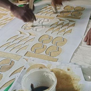 Hands painting a pattern in dark mud onto cotton cloth