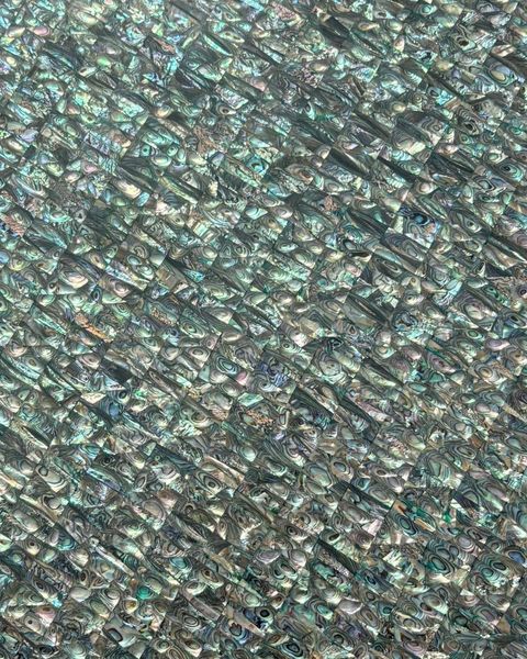Close-up of a finished surface of hundreds of small abalone tiles in green, blue and silver