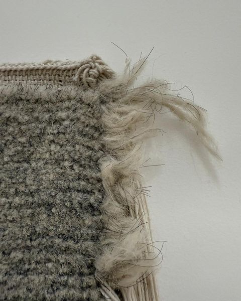 Close-up of the edge of a woven panel, fine dark hairs standing out from the pale weave