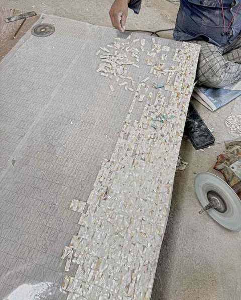 A craftsman setting small tiles of mother of pearl along a drawn grid on a large panel