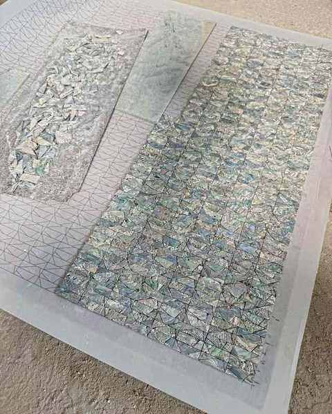 Panels of abalone mosaic laid on a grid on the workshop floor