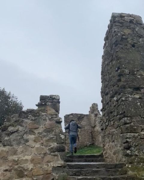 A man climbing stone steps between the ruined walls of a fortress under a grey sky