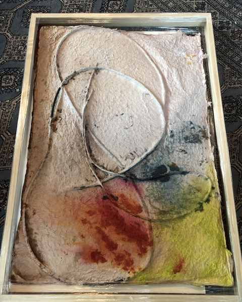 A lokta paper work in pink, red, yellow and grey with cords pressed into it, in a pale wood frame