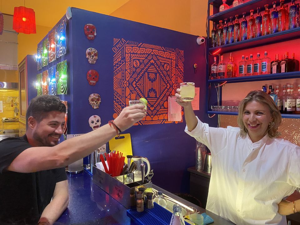 Chef Tekuna Gachechiladze behind a bar, raising a glass in a toast with a guest