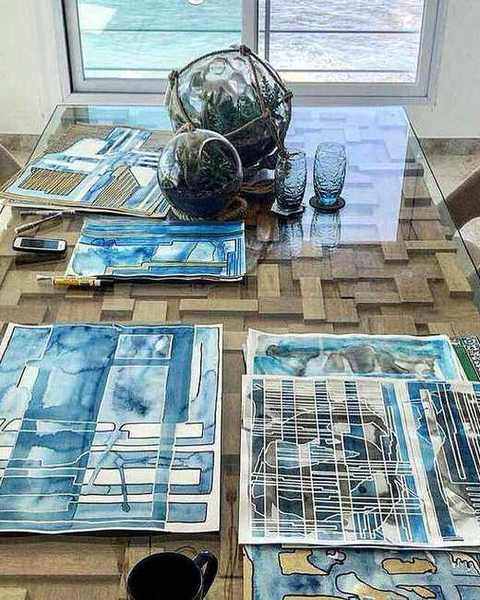 Blue watercolour drawings spread on a table by a window over the sea
