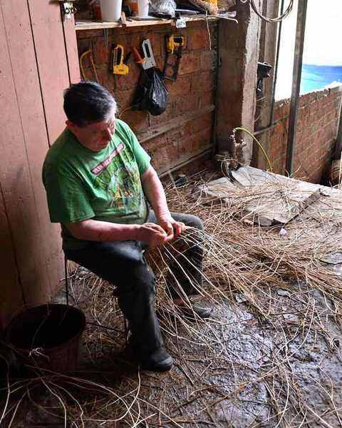 A weaver seated among loose straw, weaving a basket by hand