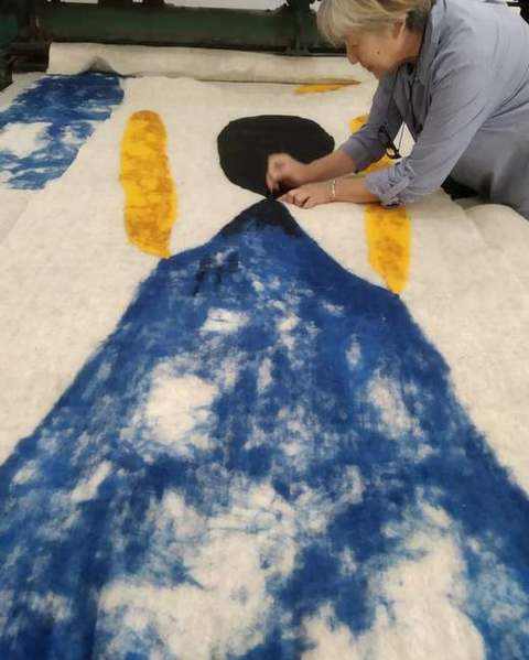 A felt-maker shaping the black head of a blue and yellow figure in loose wool