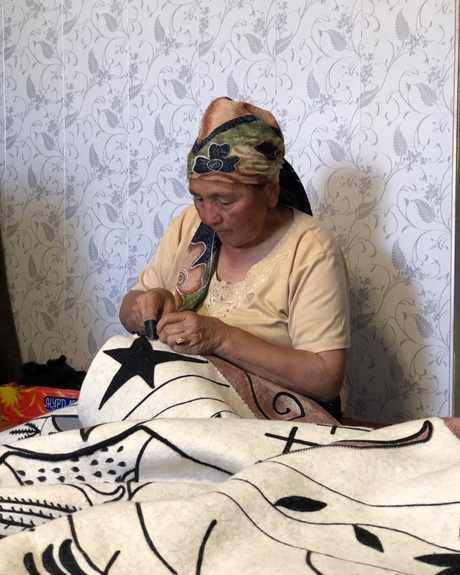 A felt-maker in a headscarf stitching the black line of a drawing into white felt