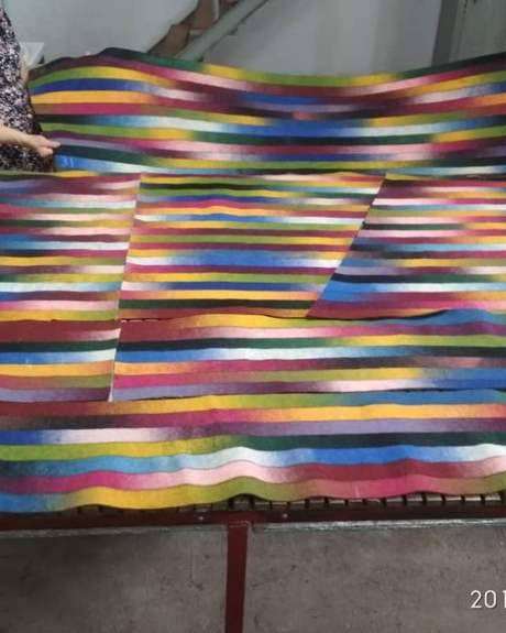Two felt-makers holding up panels of striped felt in graded colours