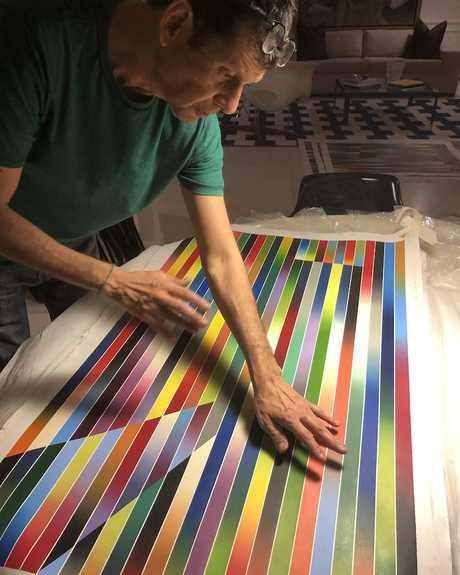 Fabian Burgos leaning over one of his striped prints on a table in Miami