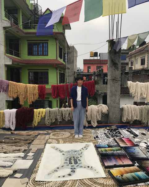 Aya Takano standing on a rooftop by her snow-leopard drawing, with dyed wool and colour boxes around her