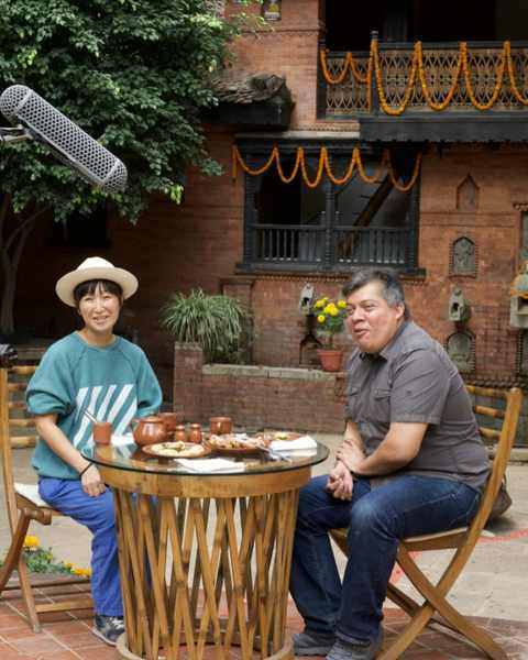 Aya Takano and Vargas-Suárez Universal interviewed at a table in a brick courtyard, a boom microphone above