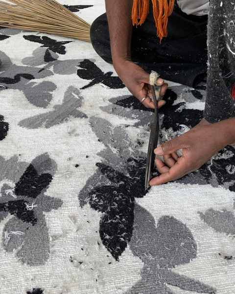 A carver trimming the pile around black and grey butterflies on a white hand-knotted work