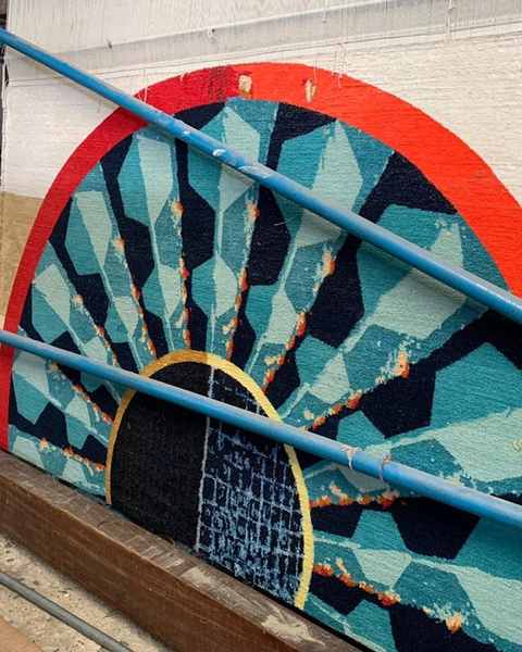 A half-circle of red, turquoise and black emerging on a vertical loom