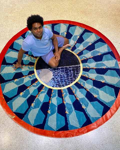 A round hand-knotted work with a red rim, turquoise rays and a city grid at its centre