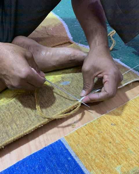 Hands binding the yellow edge of a shaped work with a needle and thread