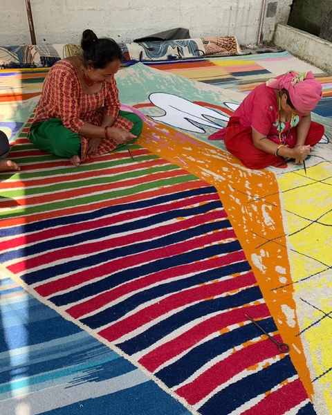 Four people seated on a large striped hand-knotted work, carving the pile