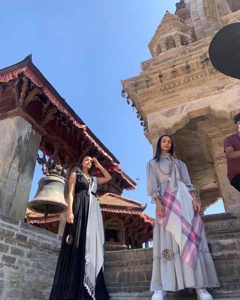 Two models on temple steps in Bhaktapur, one in black with a white shawl, one in grey with a pink check shawl