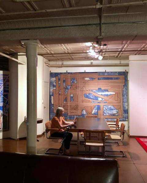 Carla Stellweg seated at a table in front of a blue and brown work and a red work that runs onto the floor