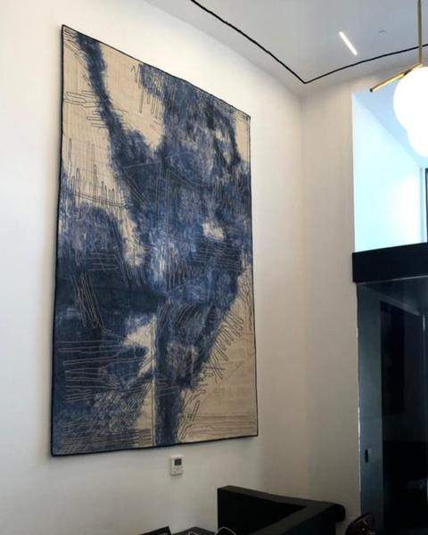 A tall blue and white textile work by Vargas-Suárez Universal hung in a double-height building lobby