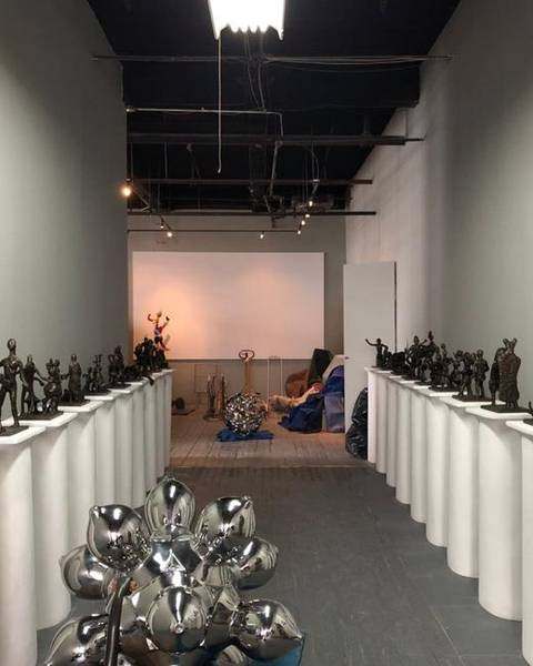 Saint Clair Cemin in his Brooklyn studio beside rows of bronze figures on white plinths and a polished steel sculpture