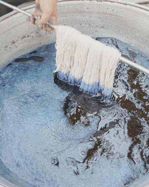 White silk skeins on a rod entering a vat of indigo