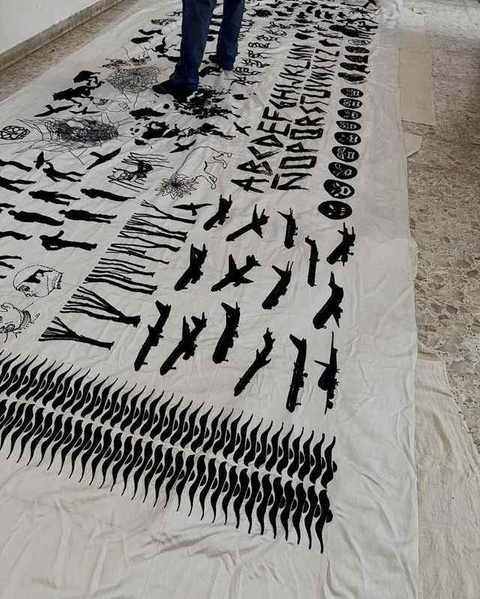 The finished suzani unrolled on the floor, rows of black silhouettes, aeroplanes and an alphabet