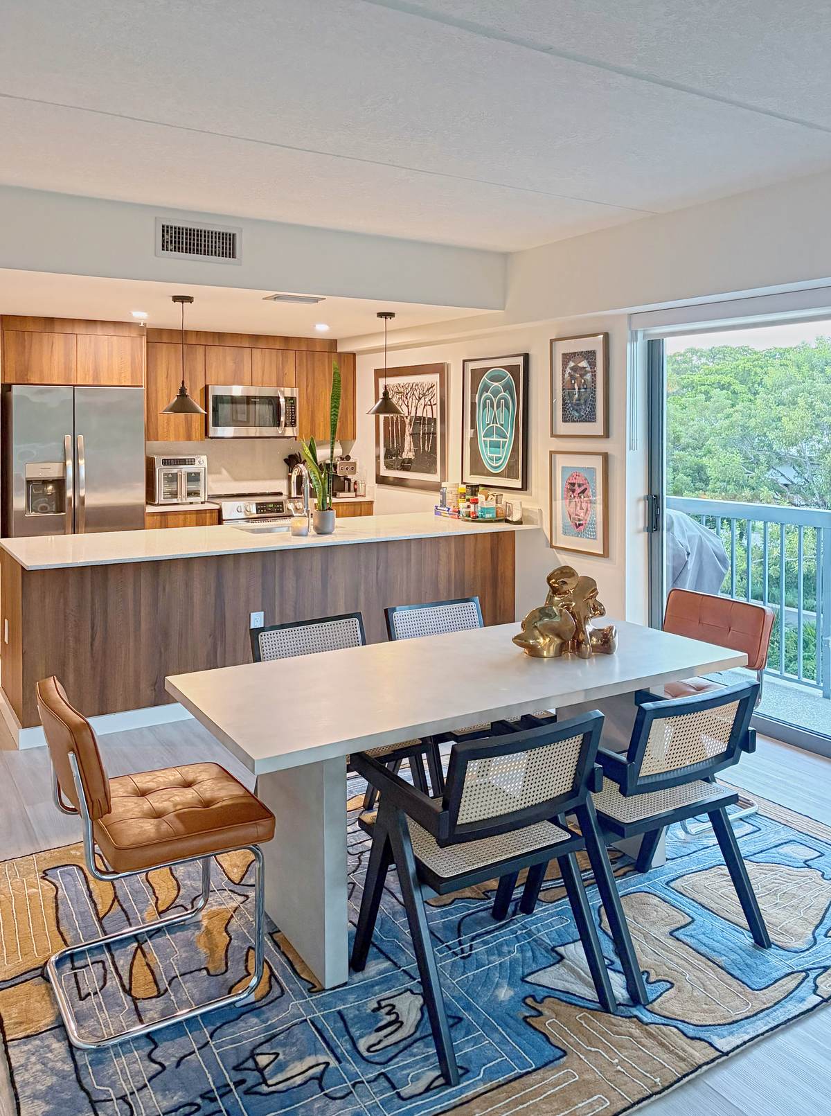 Dining table with caned chairs and a gold sculpture, framed works on the kitchen wall