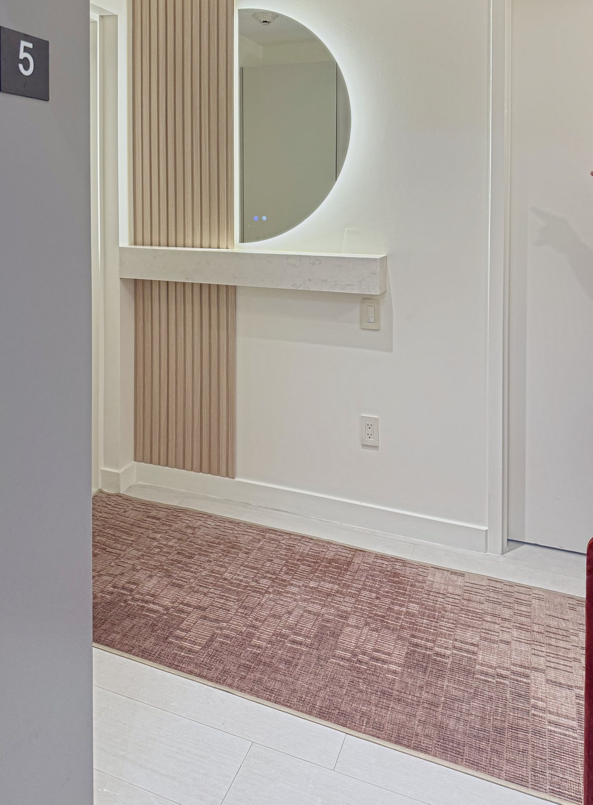 The entry: a round backlit mirror on fluted oak and a floating shelf
